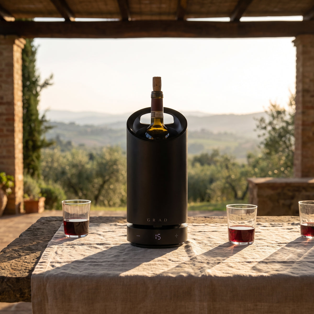 GRAD No.1 Black Edition holding a bottle of red wine at 15 °C on a terrace table overlooking Tuscan hills